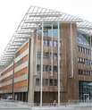 Large building built out of light brown wood. The building's top is roundly shaped and has a fence-looking layer. It is also connected to another similar looking building through two small bridges.