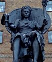 A large black statue of a woman holding two objects.