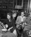 black and white photo of four elder men and one woman sitting in a living room and chatting.