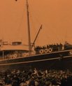Large ship arriving at the shore with a large crowd of people cheering and waiting for them